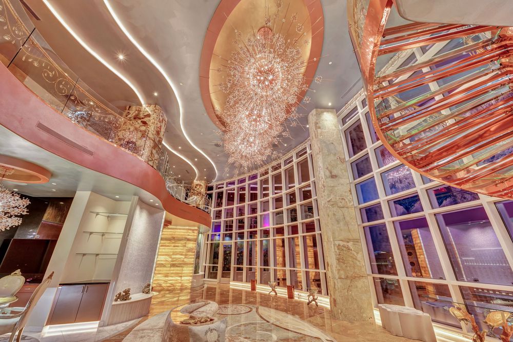 Stunning multi-story luxury interior with crystal chandelier, floor-to-ceiling windows, and rose gold accents.
