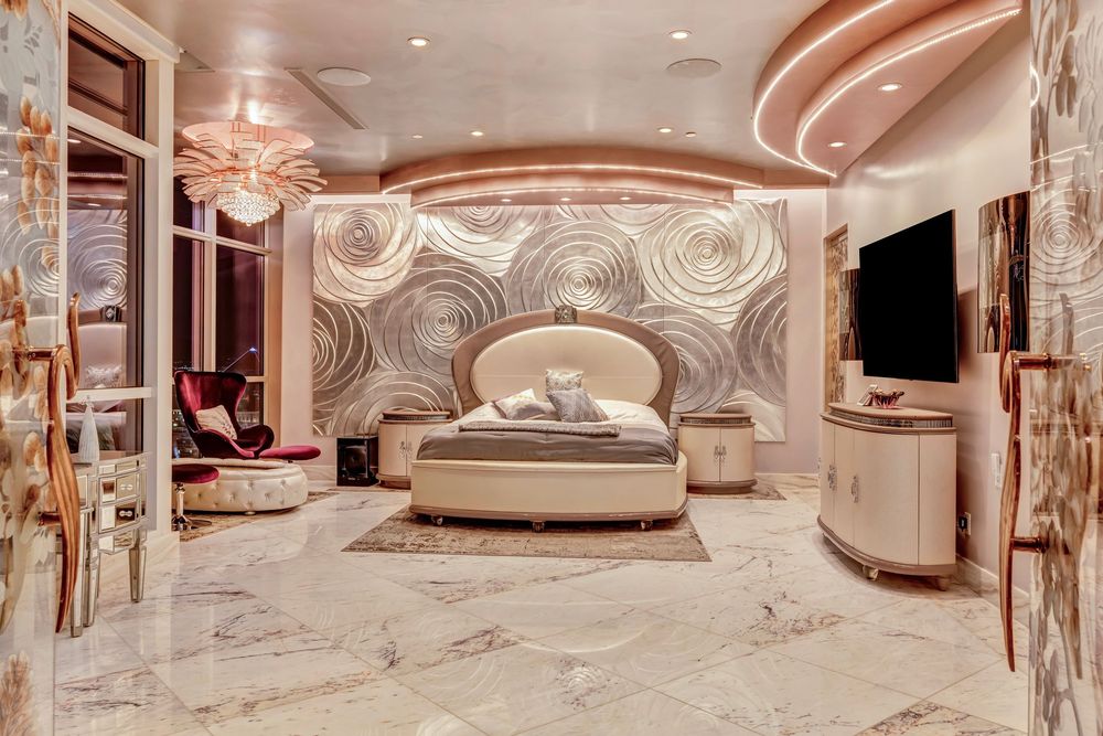 Opulent master bedroom with circular bed, decorative wall art, marble floors, and recessed lighting.