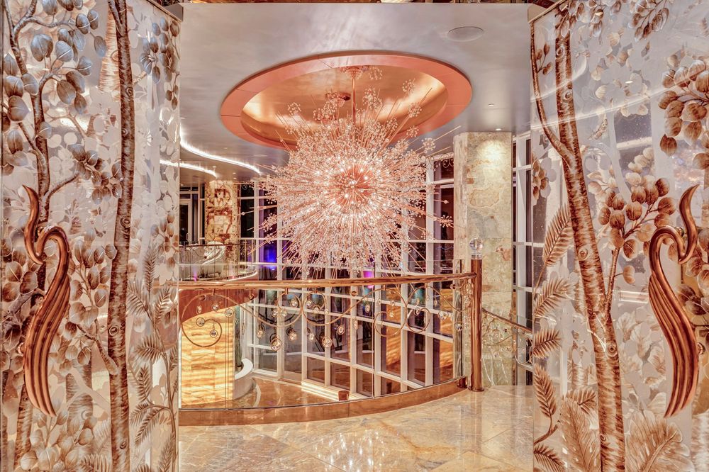 Glamorous entryway with ornate floral wall panels, rose gold chandelier, and reflective marble flooring.