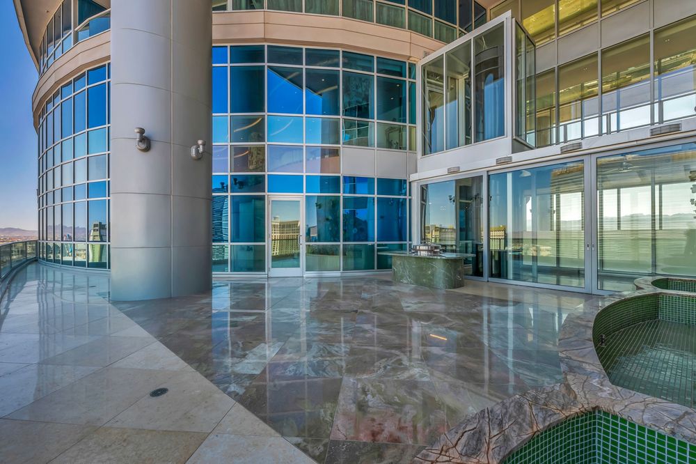 Modern high-rise penthouse terrace with polished marble floors, glass walls, and panoramic city views.