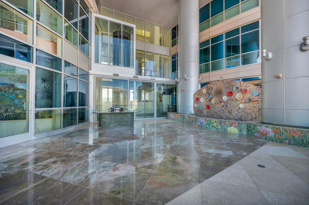 Spacious luxury building lobby with polished marble floors, floor-to-ceiling glass walls, and mosaic art.