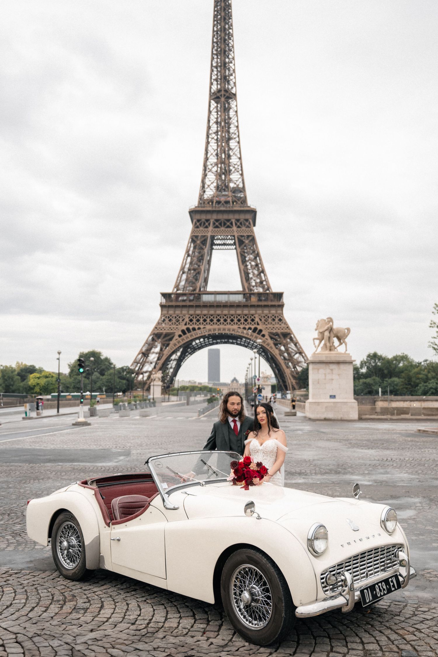 Romantic couple poses by vintage white car in front of Eiffel Tower in Paris on misty morning.