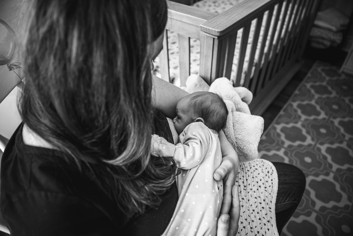 A black and white view from above of someone holding a baby dressed in white beside a crib.