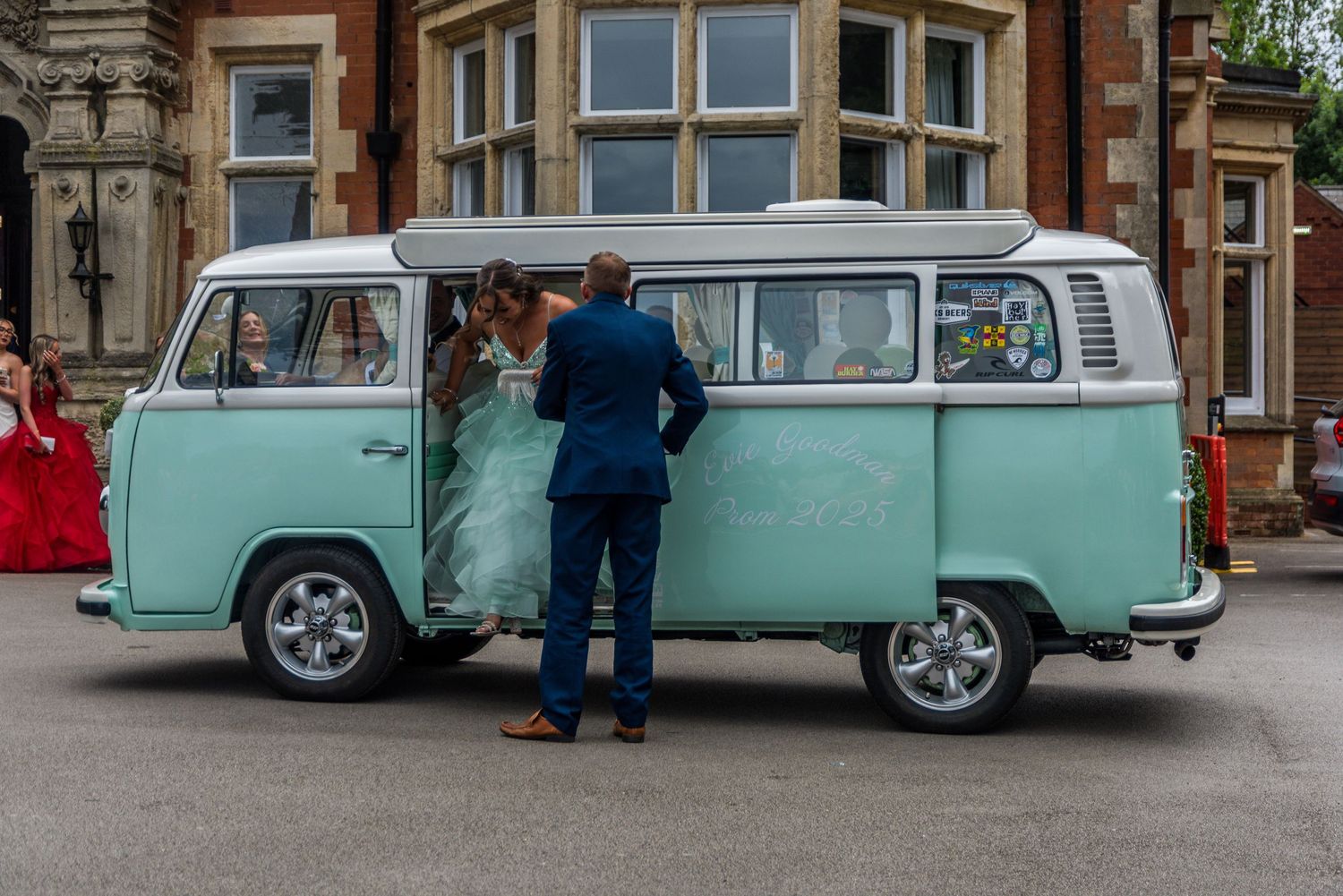 A mint green vintage Volkswagen bus serves as a wedding vehicle, with someone in blue assisting by the door.
