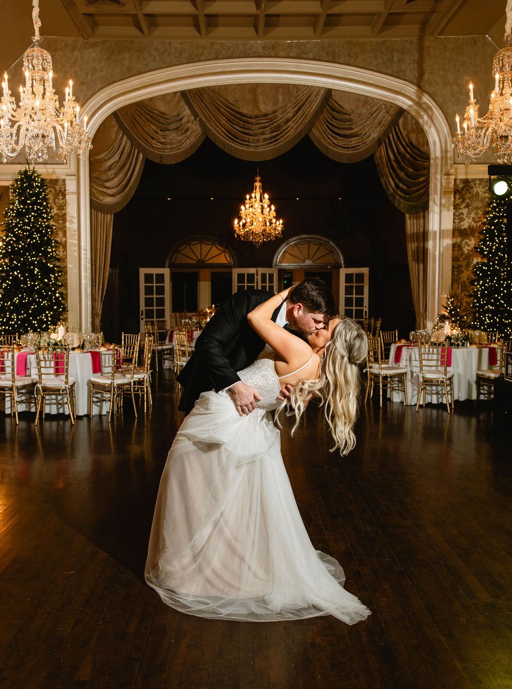A romantic ballroom dance dip captured in an elegant venue with chandeliers and Christmas trees. Merion Cricket Club Wedding.