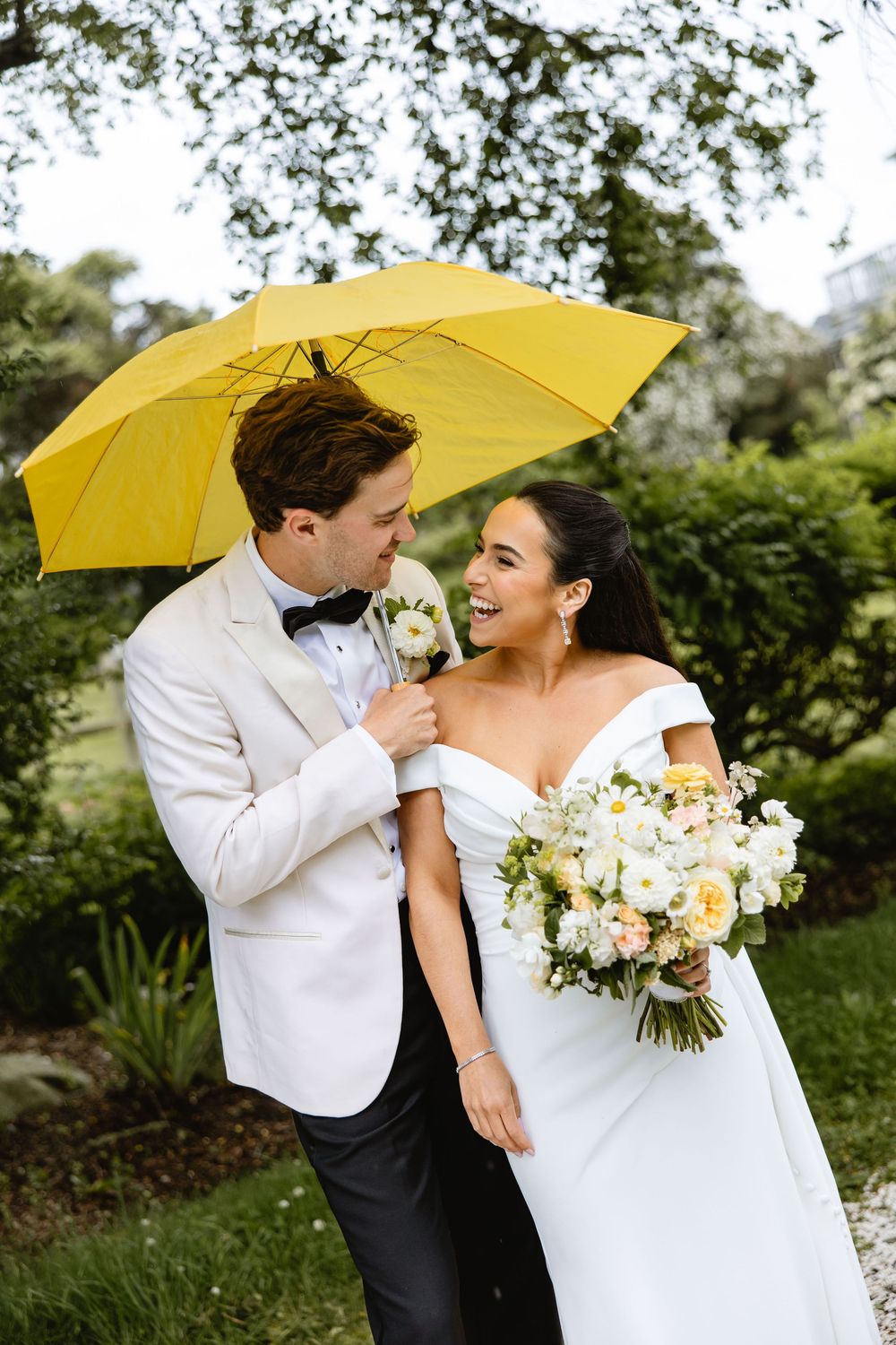 Couple sharing intimate moment under yellow umbrella with white floral bouquet. Nonquitt beach. New England wedding.