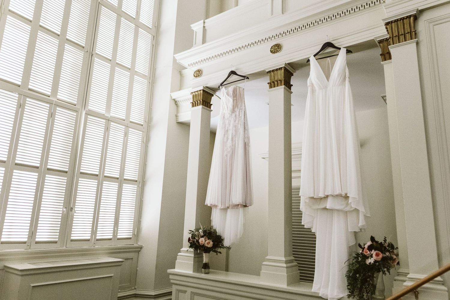 White wedding dresses hanging in a bright sunlit room with large windows.