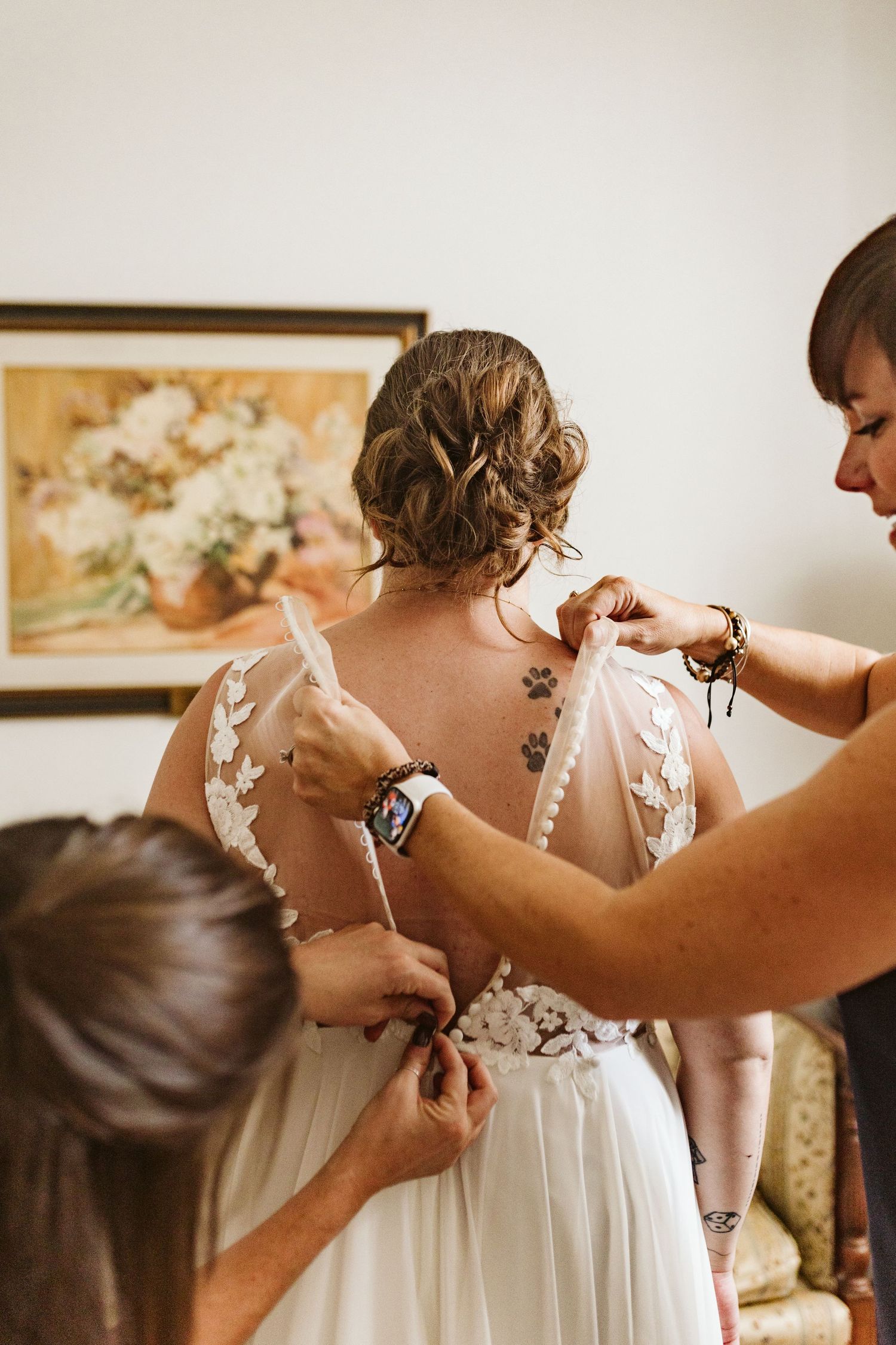 Someone helps fasten the back of a delicate white wedding dress with lace details.