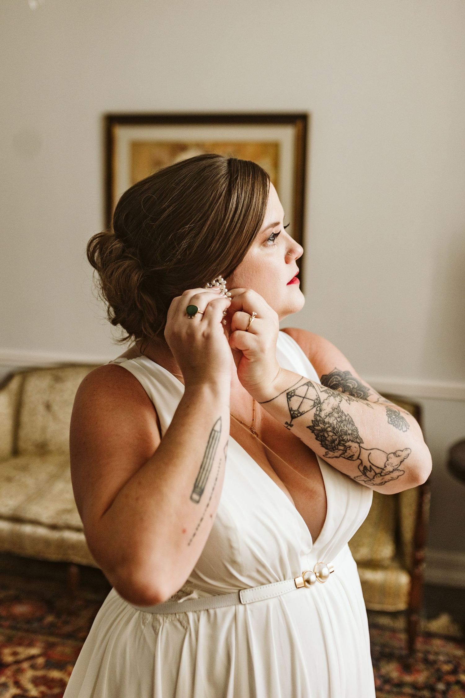 A person in a white wedding dress puts on earrings while getting ready.