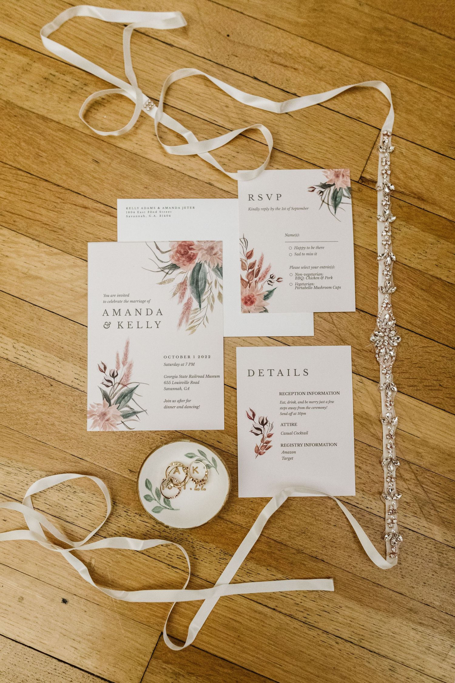 Wedding invitation suite with floral designs and white ribbons laid out on wooden flooring.