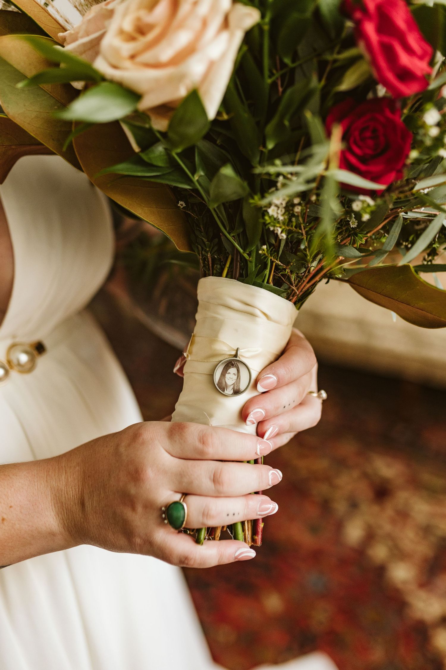 Close-up of hands wearing rings and holding a bouquet with red and pink roses.