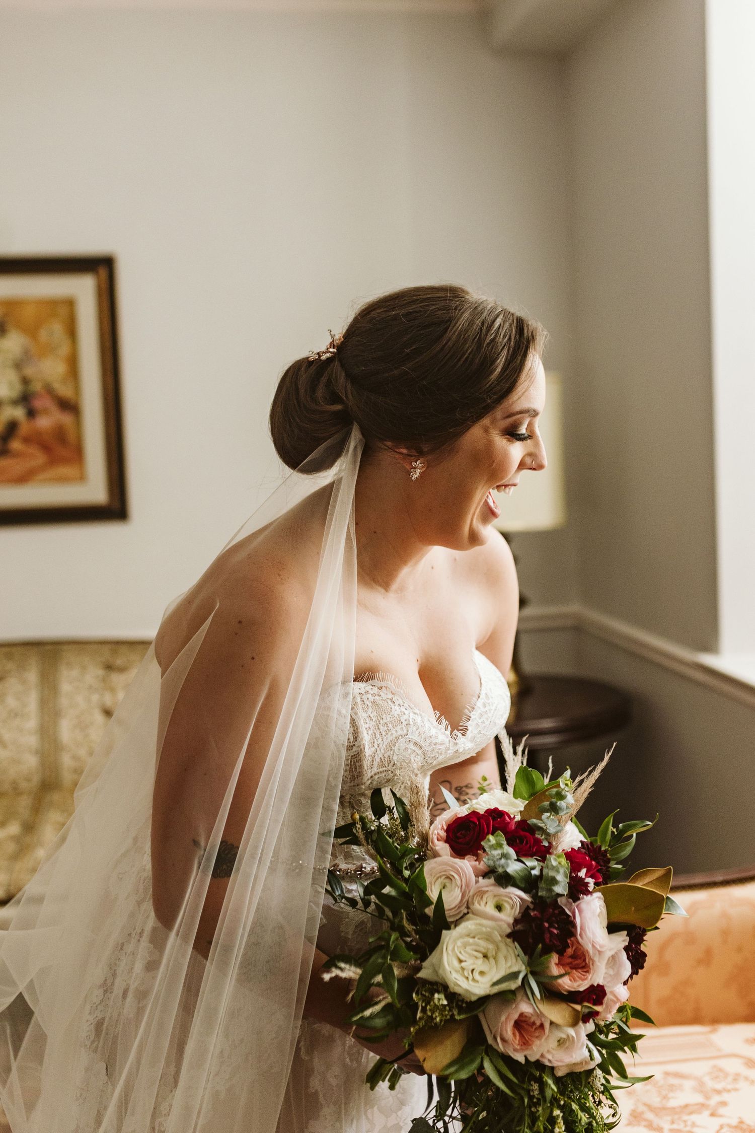 A bride wearing a flowing veil poses with her wedding bouquet in an elegant indoor setting.