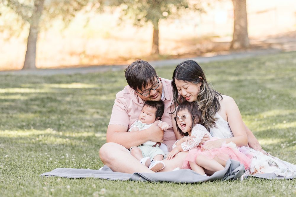 Family sits together on blanket sharing laughs on sunny grass.
