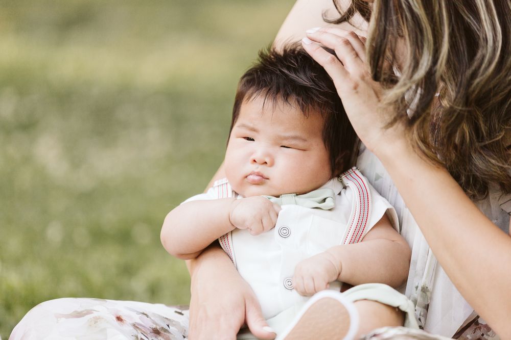 A sleeping baby rests peacefully against someone outdoors in natural lighting.