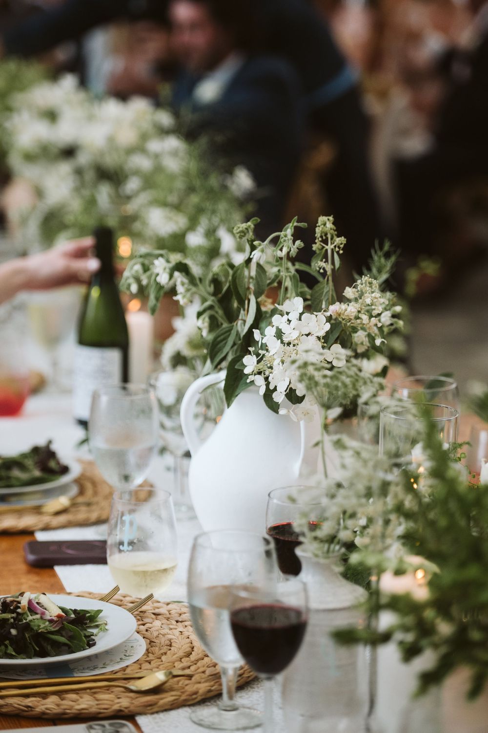 Elegant wedding table setting with white floral centerpiece, wine glasses, and greenery on a wooden table.