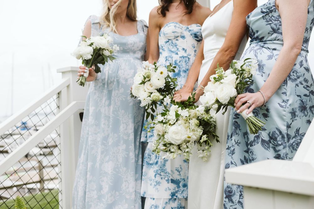 Bridesmaids in blue floral dresses holding white bouquets on outdoor staircase.