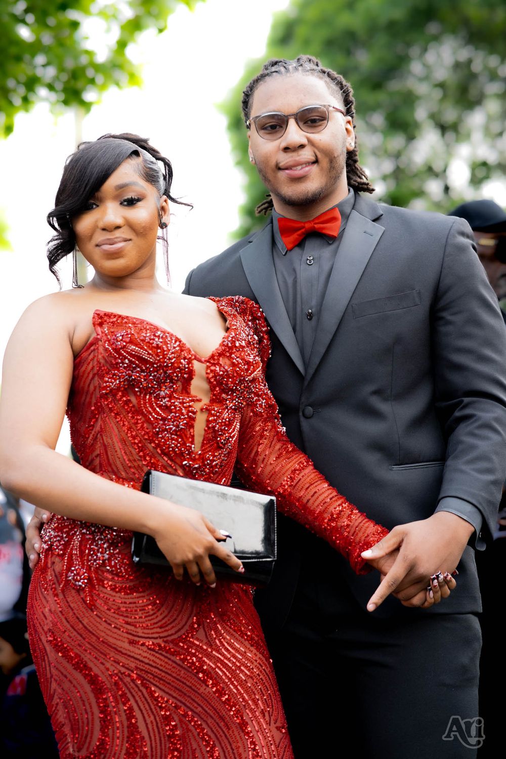 Formal couple in red dress and black tuxedo posing together for prom or event photo.