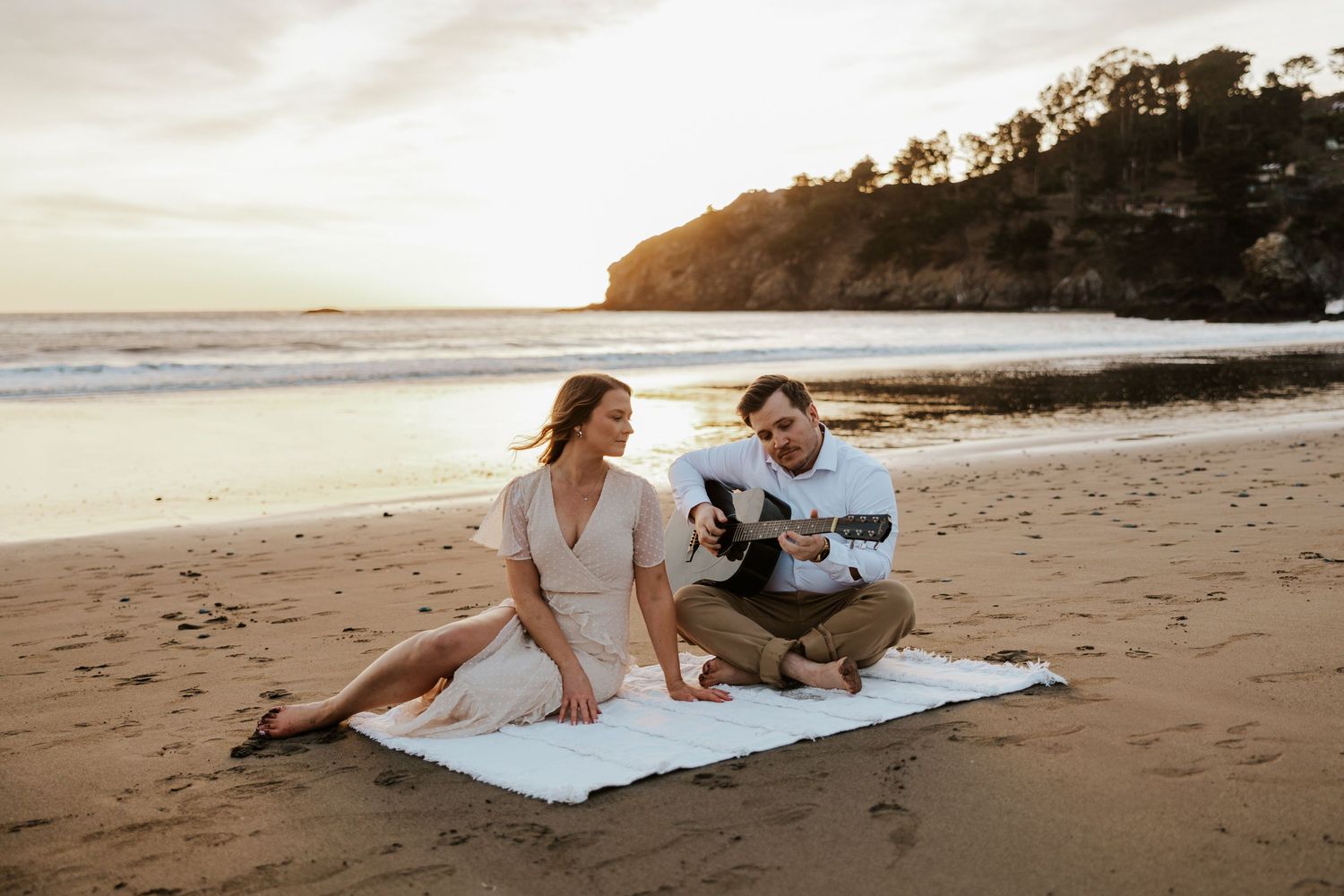 couple sitting on a beach with the man playing guitar to his lady during their engagement session