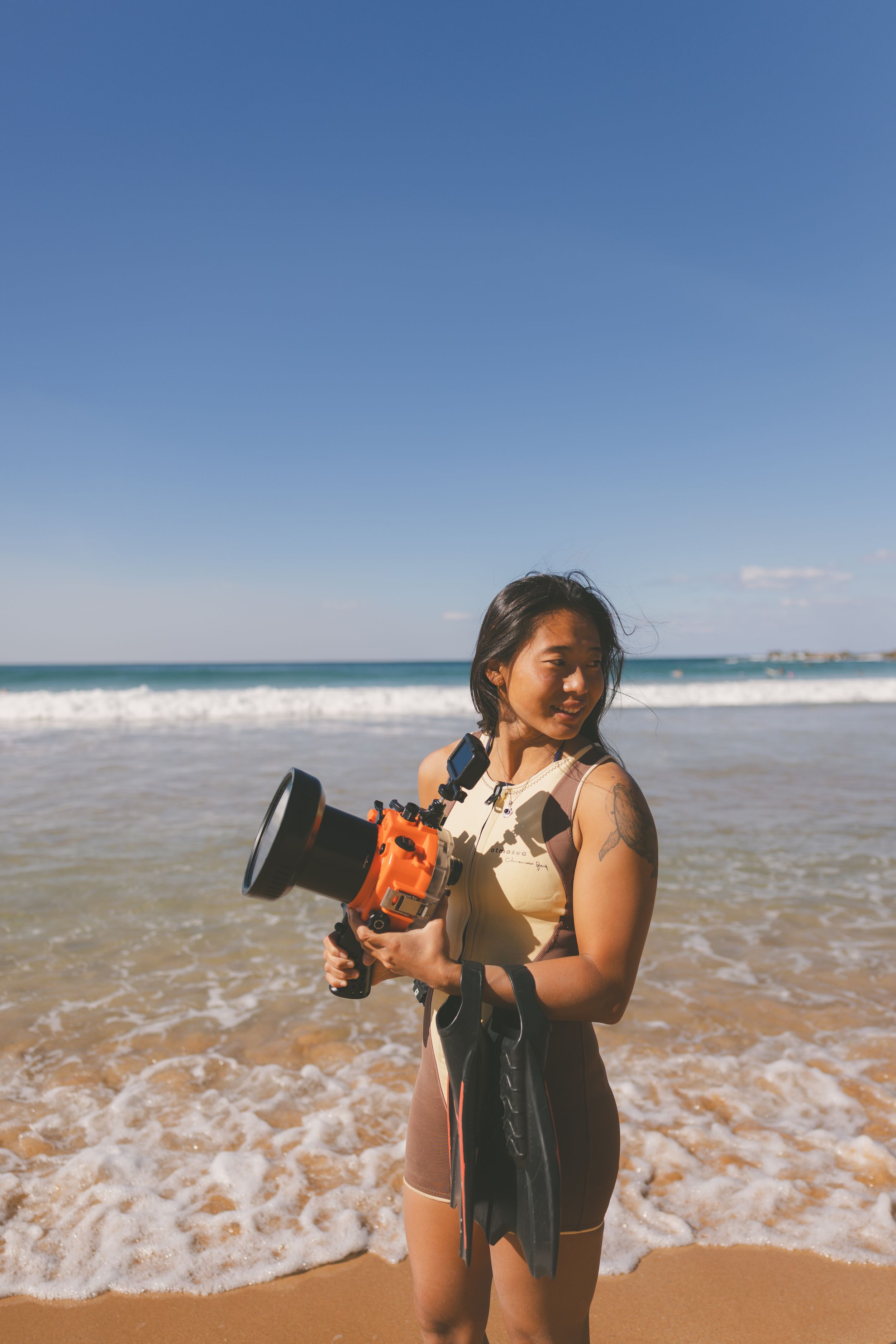 Portrait of a female surf photographer looking back at the ocean ready to swim into the surf with her flippers on hand at Newcastle, NSW
