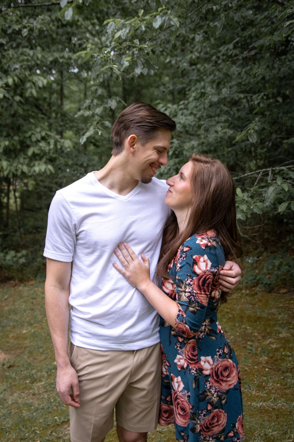 Couple gazing lovingly at each other outdoors, woman in floral dress touching mans white t-shirt chest.