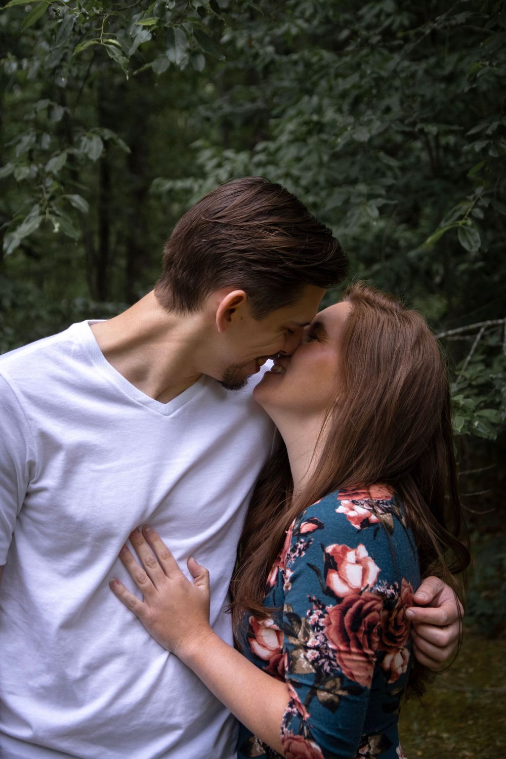 A young couple sharing a romantic kiss outdoors surrounded by lush green forest trees.
