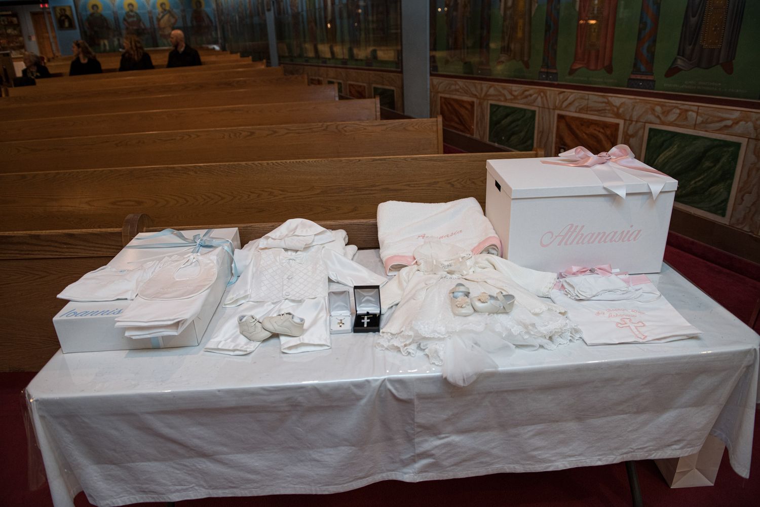 White christening outfits and gift boxes arranged on a table inside a church.