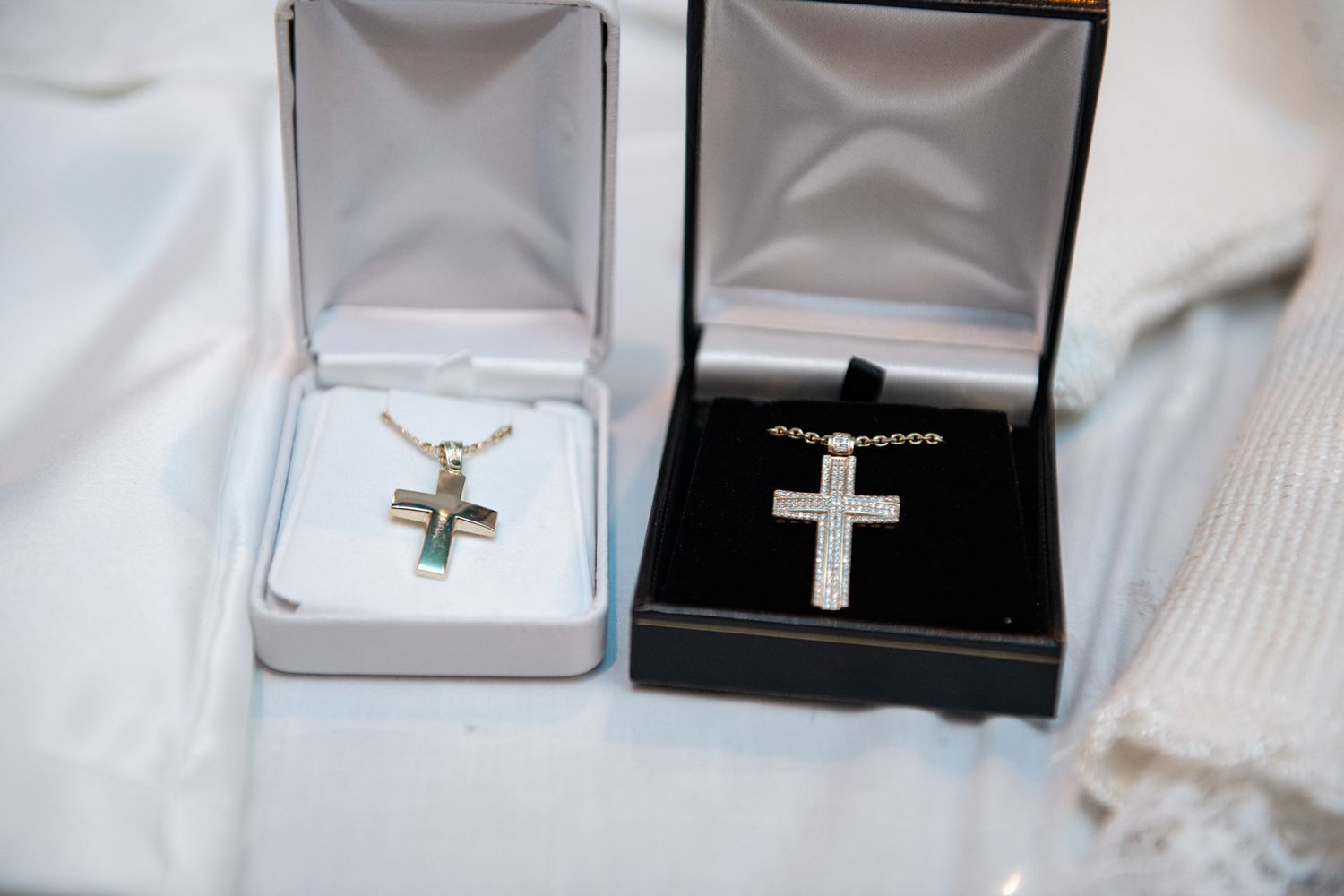 Two silver cross necklaces in open jewelry boxes on a white cloth at a christening.