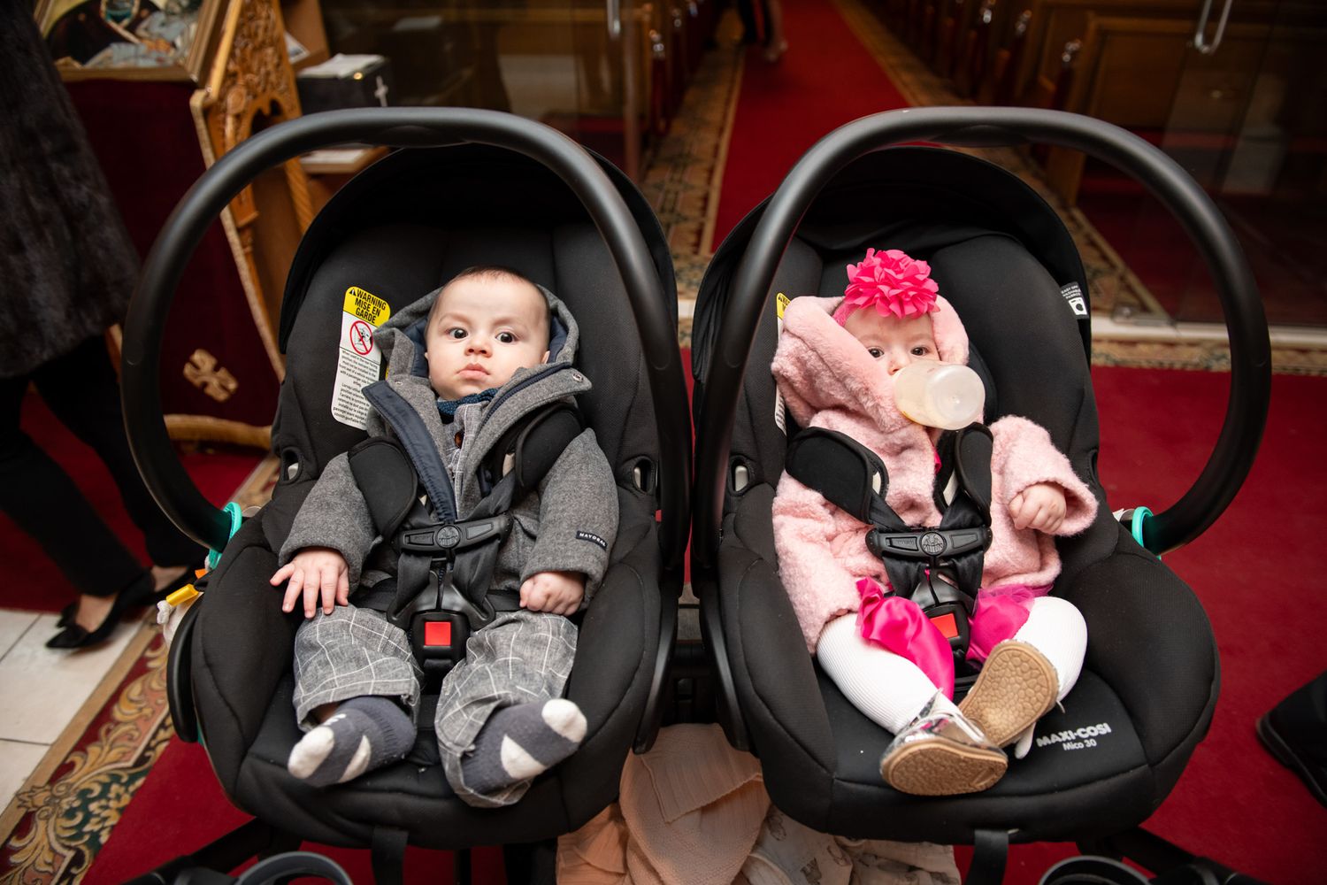 Two babies in black infant car seats side by side inside a church.