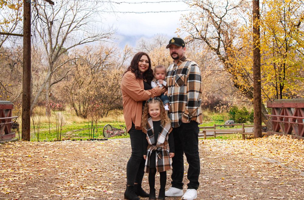 Family of four poses on autumn trail with colorful fall foliage during outdoor family portrait session.