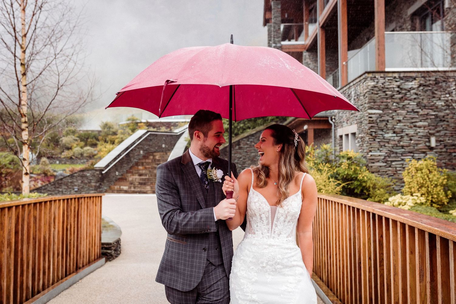 Bride and groom laugh at each other as they cross the bridge in the rain at Lodore Falls Hotel