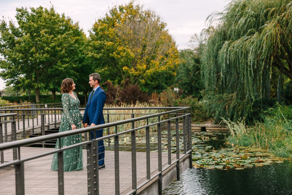 A bride in a green dress and groom in a blue suit share a quiet moment on the boardwalk of the Greater Des Moines Botanical Garden.
