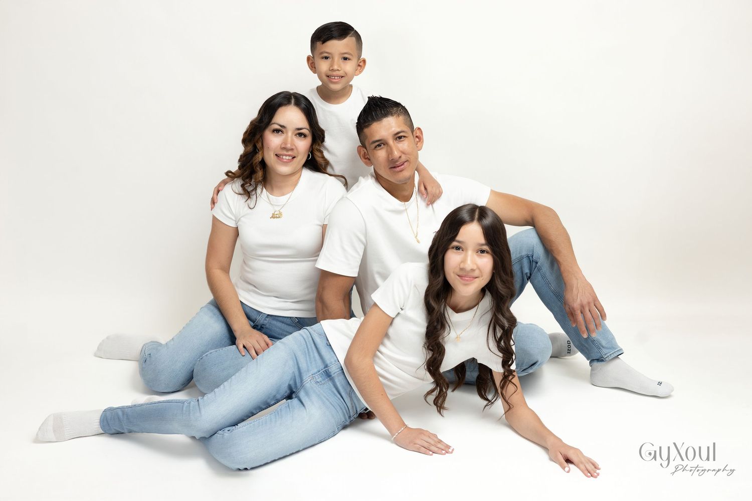 Family of four in matching white tops and jeans posing together against a white background in a professional photo.