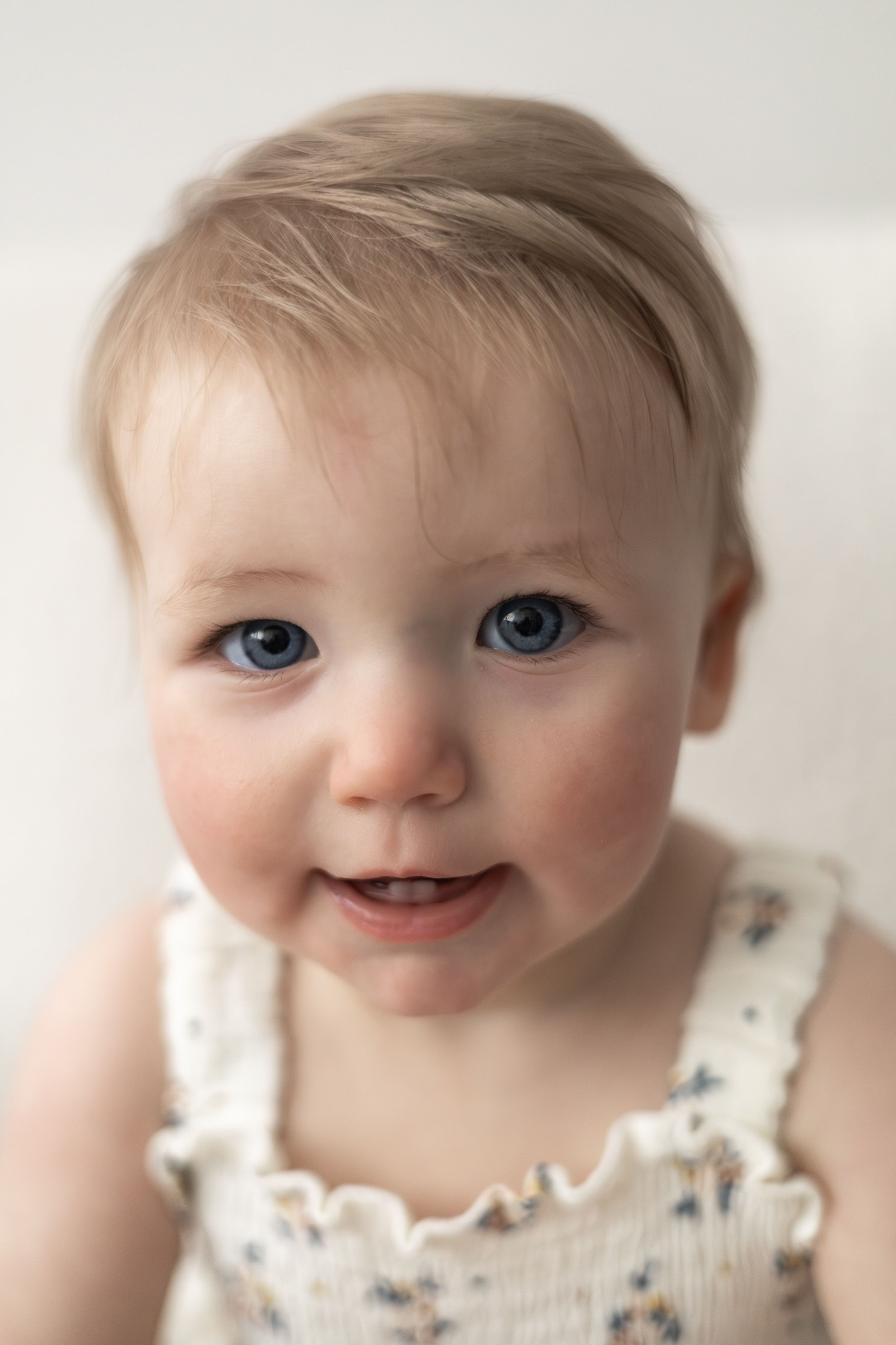 Adorable baby with blue eyes and blonde hair smiling, wearing a white outfit Nottingham birthday photography baby turning one