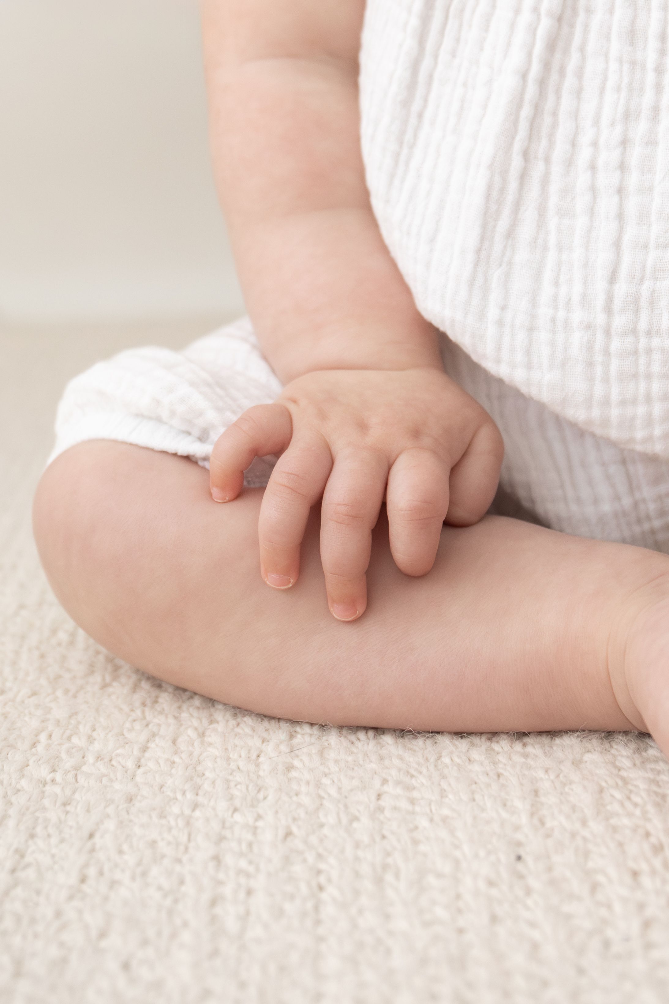Close-up of a baby's hand resting on their knee while sitting cross-legged on a soft cream carpet birthday photography Nottingham