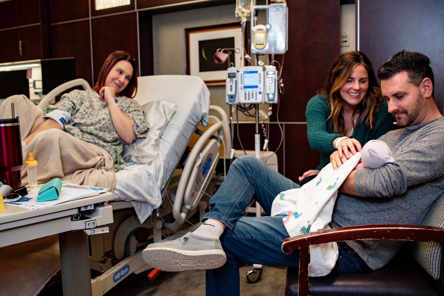 Hospital room scene shows parents and newborn sharing quiet moments together.