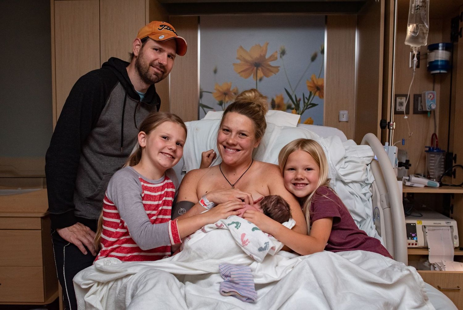 Happy family poses together with newborn in hospital room.