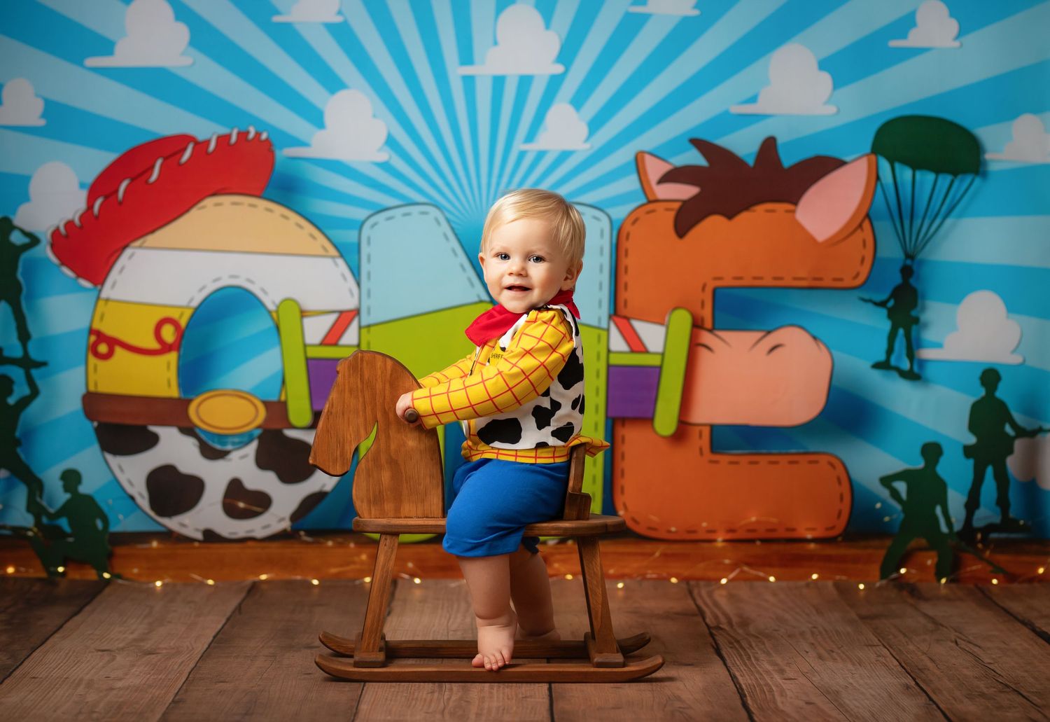 Baby in Woody costume sits on rocking horse chair before Toy Story ONE backdrop for first birthday cake smash photo.