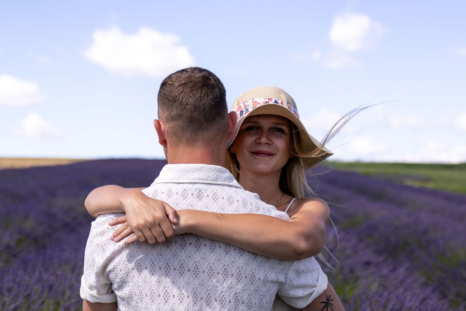 Couple embracing in a lavender field, woman in a hat smiling, romantic outdoor photography.