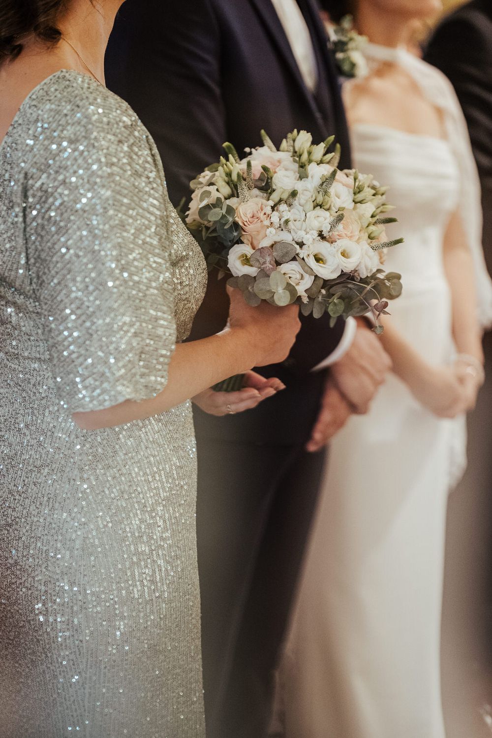 Wedding party close-up with bride in white gown and guest holding elegant white floral bouquet.