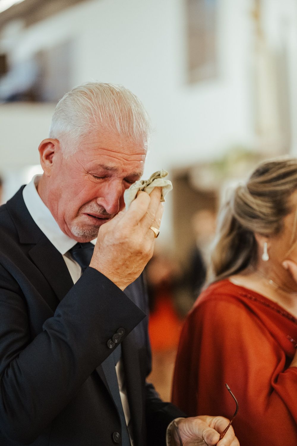 Emotional elderly man in suit wiping tears with handkerchief at a wedding ceremony.