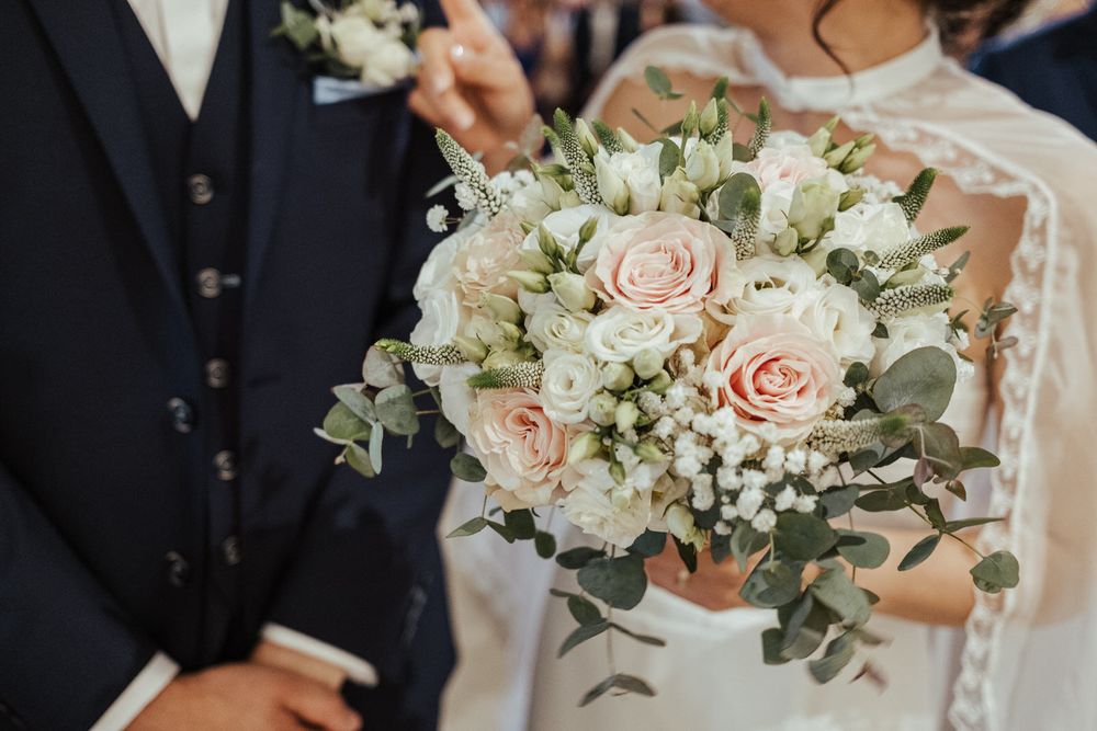 Bride and groom holding elegant wedding bouquet with pink roses, white flowers, and eucalyptus greenery.