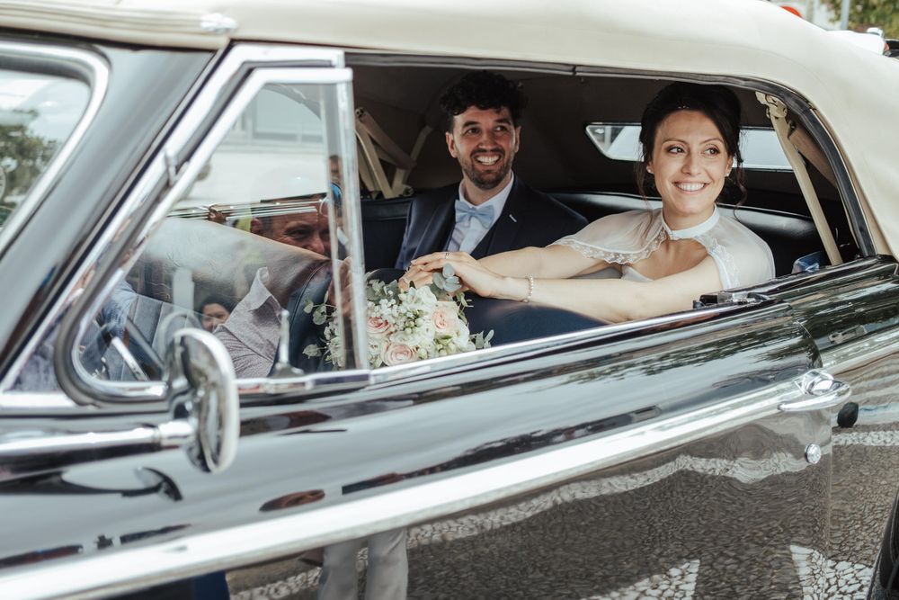 Smiling bride and groom sitting in a classic vintage white car on their wedding day.