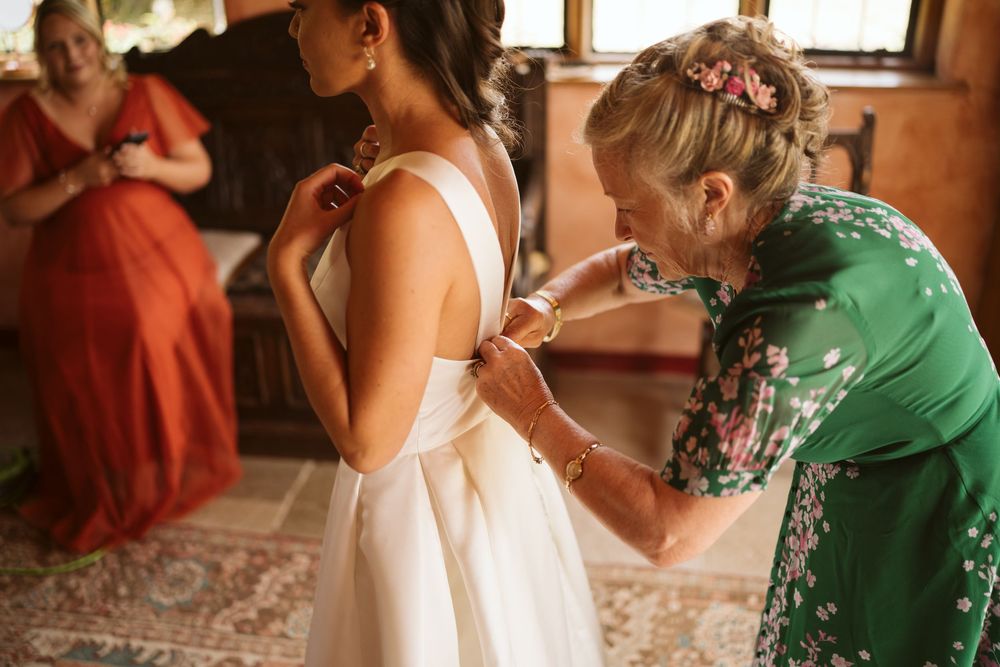 Bridesmaid lovingly fastening the bride's wedding dress before the ceremony