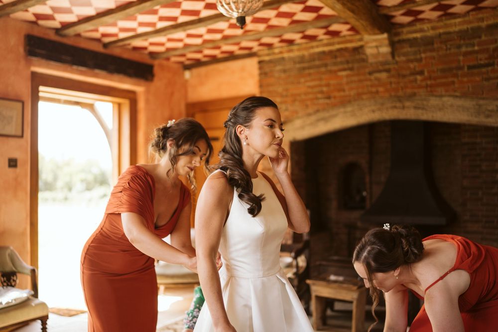 Bridesmaids helping bride get into her wedding gown on the morning of the wedding in Surrey