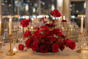 Lush red rose centerpiece with gold candlesticks on a wedding reception table with city lights backdrop at Liberty House in Jersey City, NJ.