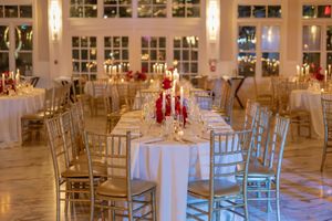 Elegant wedding reception hall with long white tables, gold chiavari chairs, red floral accents and candles at Liberty House in Jersey City.