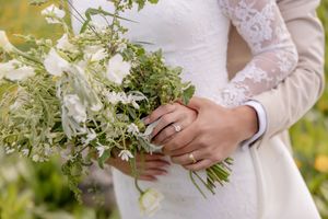 Close-up of bride and groom holding a lush white and green wedding bouquet with diamond engagement ring visible.