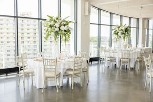 Elegant wedding reception hall with tall white floral centerpieces, chiavari chairs, and floor-to-ceiling windows at Wave Resort.