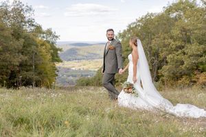 Bride and groom holding hands in a scenic meadow with rolling hills and autumn trees in the background at Mountain Creek in Vernon, NJ.