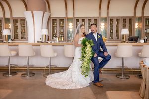 Bride and groom posing playfully in a stylish bar venue, groom in navy suit with cascading green bouquet at Wave Resort in Long Branch, NJ.
